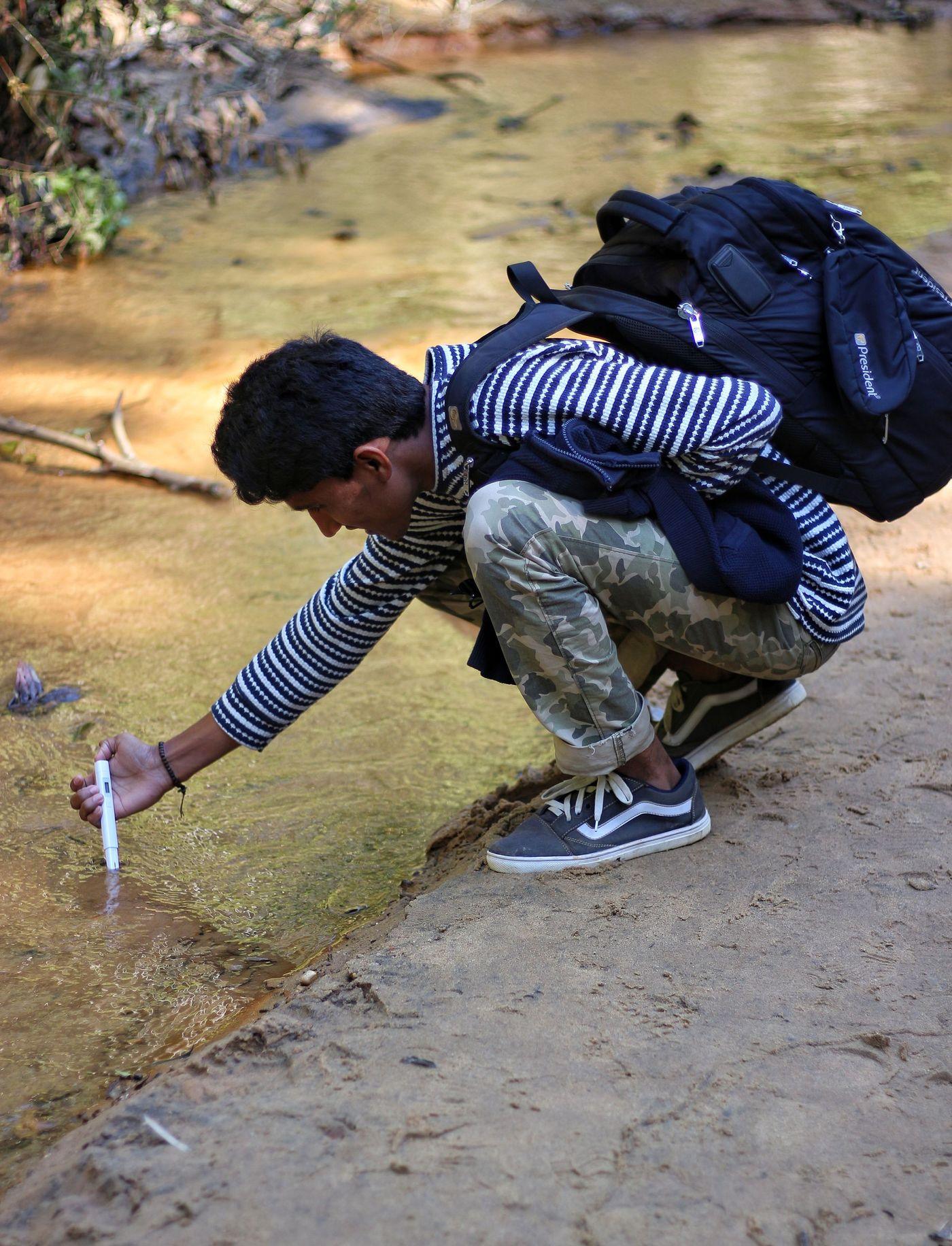 A researcher crouching at the edge of a stream, filling a sample bottle by hand